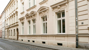 Façade ancienne rénovée avec moulures élégantes, encadrements de fenêtres raffinés et enduit clair, éclairée par une lumière naturelle douce.