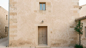 Façade d’une maison ancienne en pierre calcaire recouverte d’un enduit à la chaux beige légèrement texturé, avec des joints traditionnels visibles sous une lumière naturelle douce.